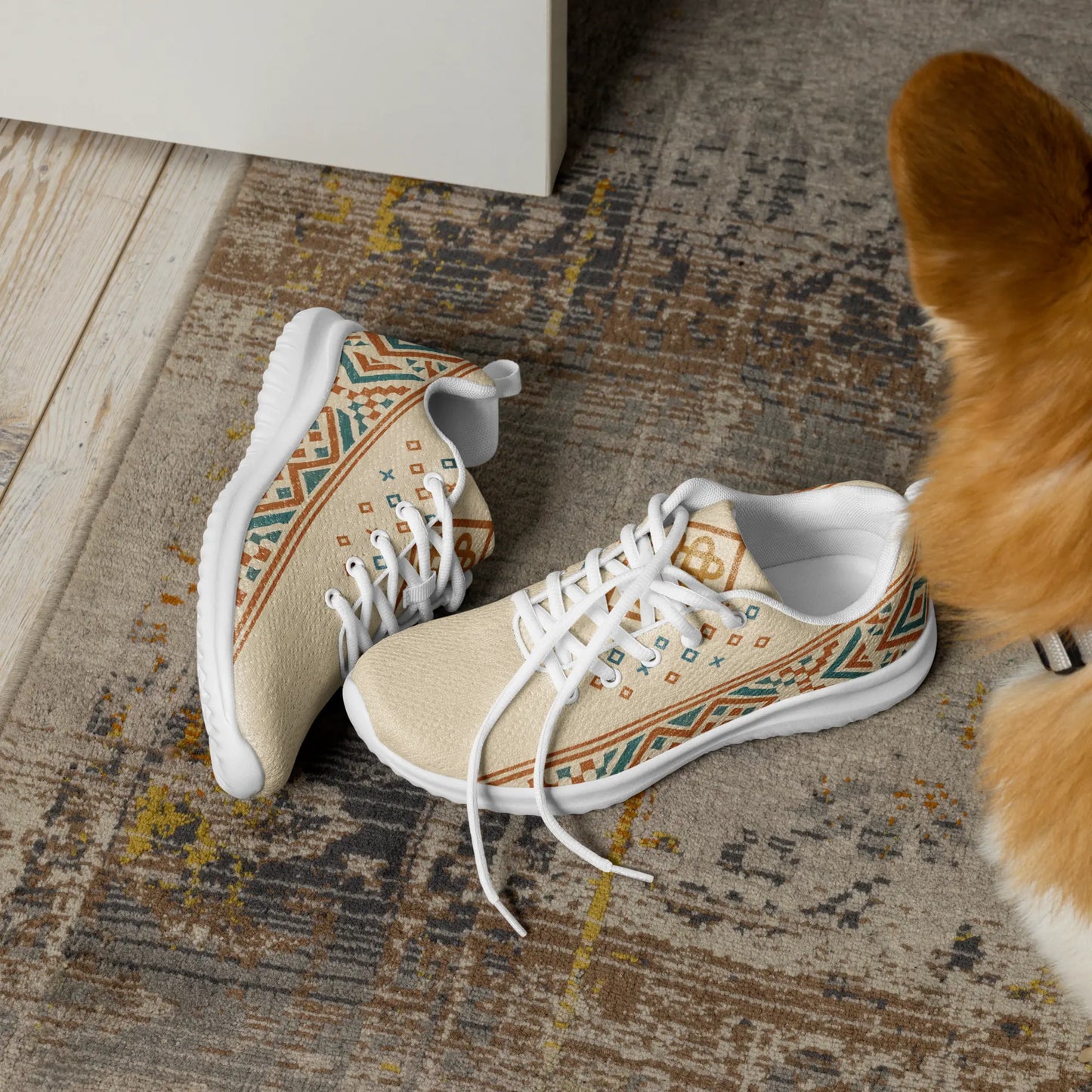 Beige men's athletic sneakers with Berber tribal pattern in teal and rust tones, shown on patterned rug with dog nearby.