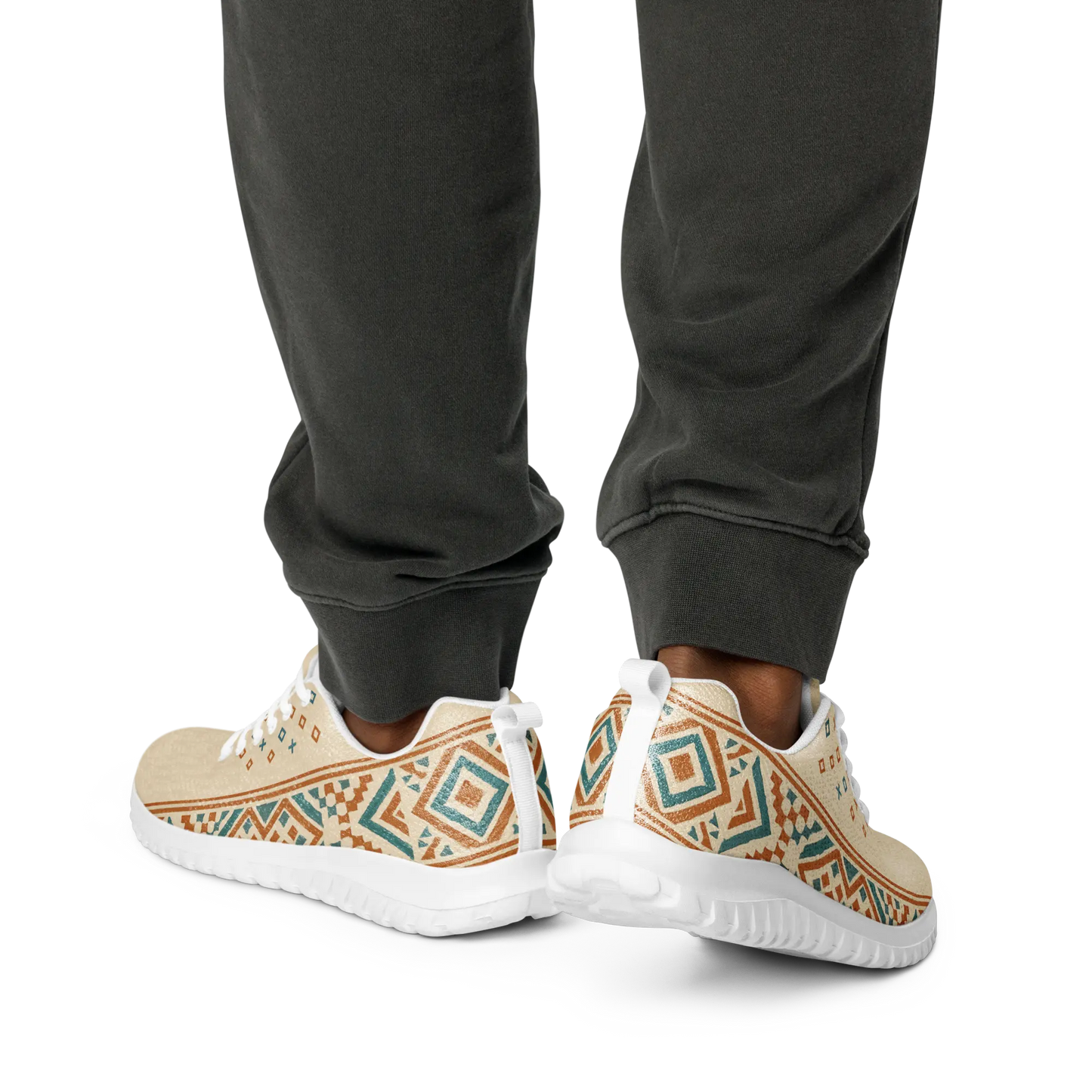 Beige men's athletic sneakers with Berber tribal pattern in teal and rust tones, shown on patterned rug with dog nearby.
