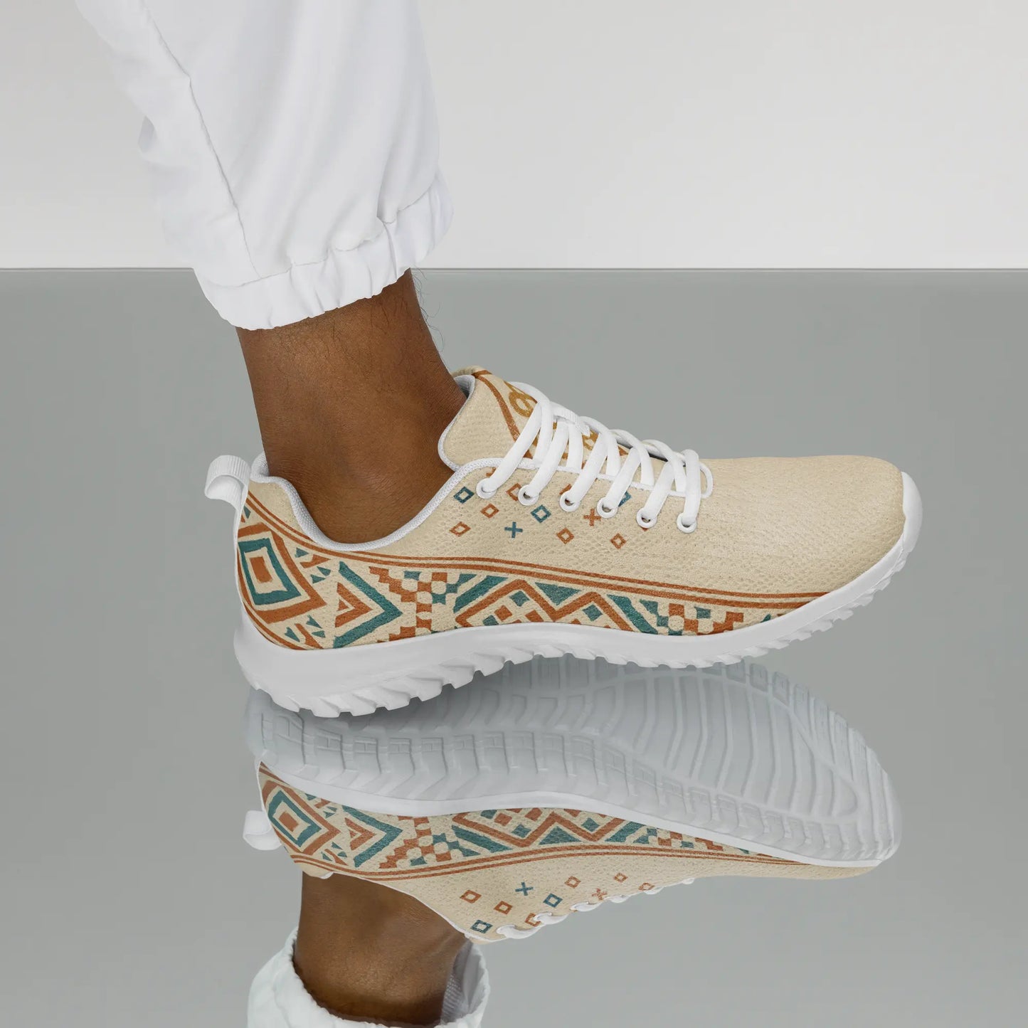 Beige men's athletic sneakers with Berber tribal pattern in teal and rust tones, shown on patterned rug with dog nearby.