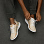Beige men's athletic sneakers with Berber tribal pattern in teal and rust tones, shown on patterned rug with dog nearby.